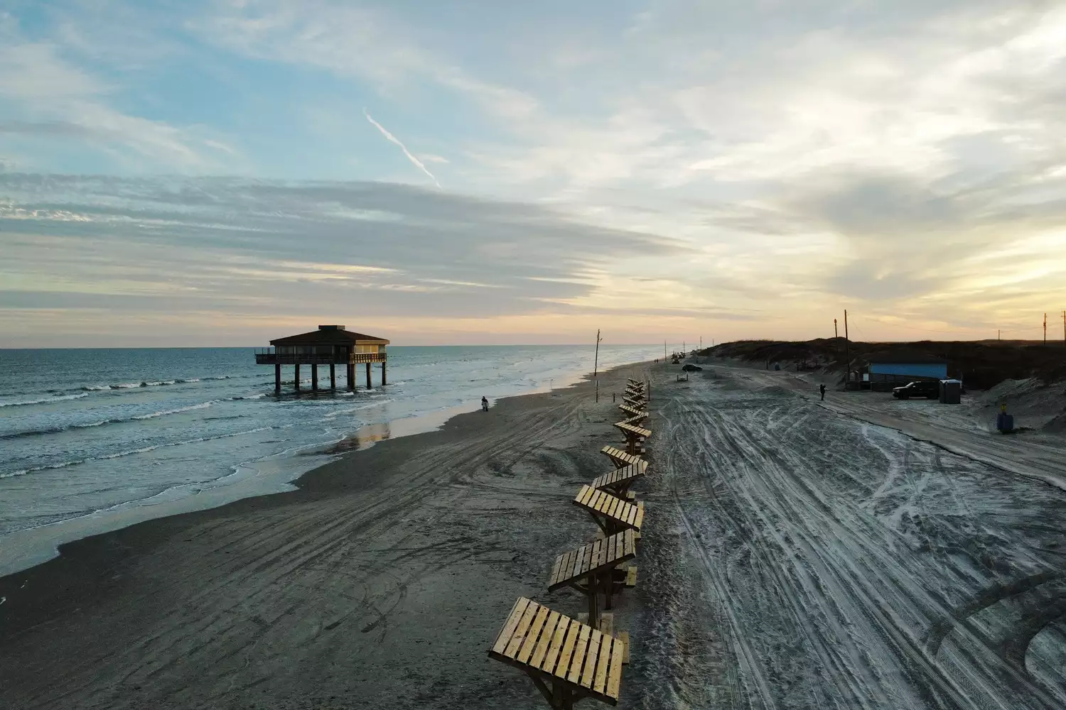 The weathered remains of a pier on the sandy shores of Padre Island under a cloudy sky.