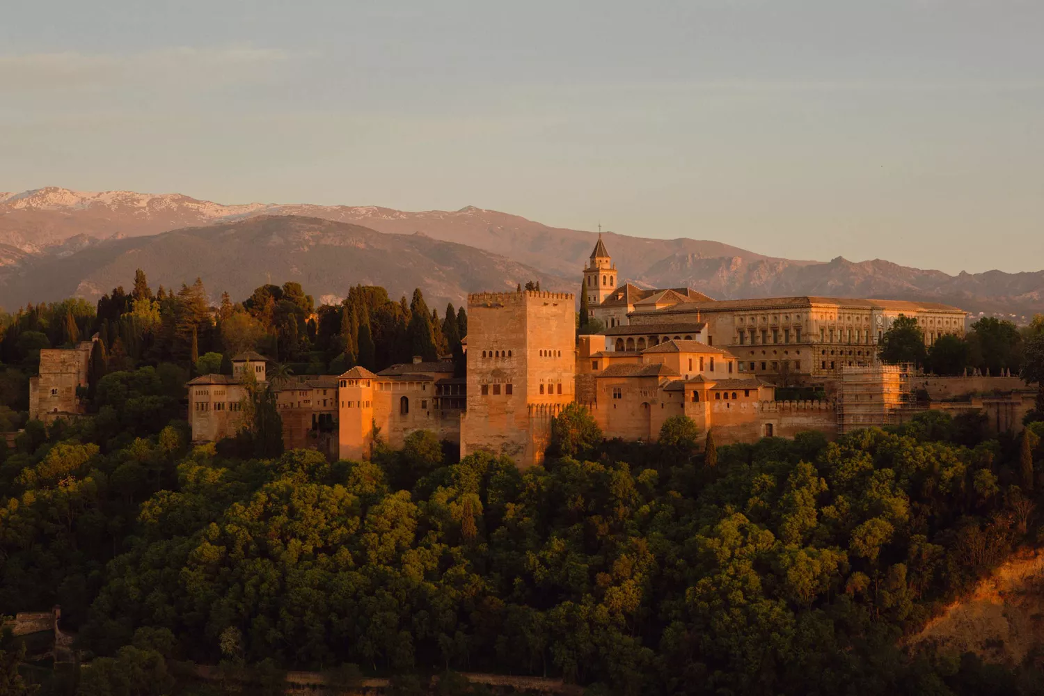The Alhambra palace and complex glowing on a hilltop during a sunset.