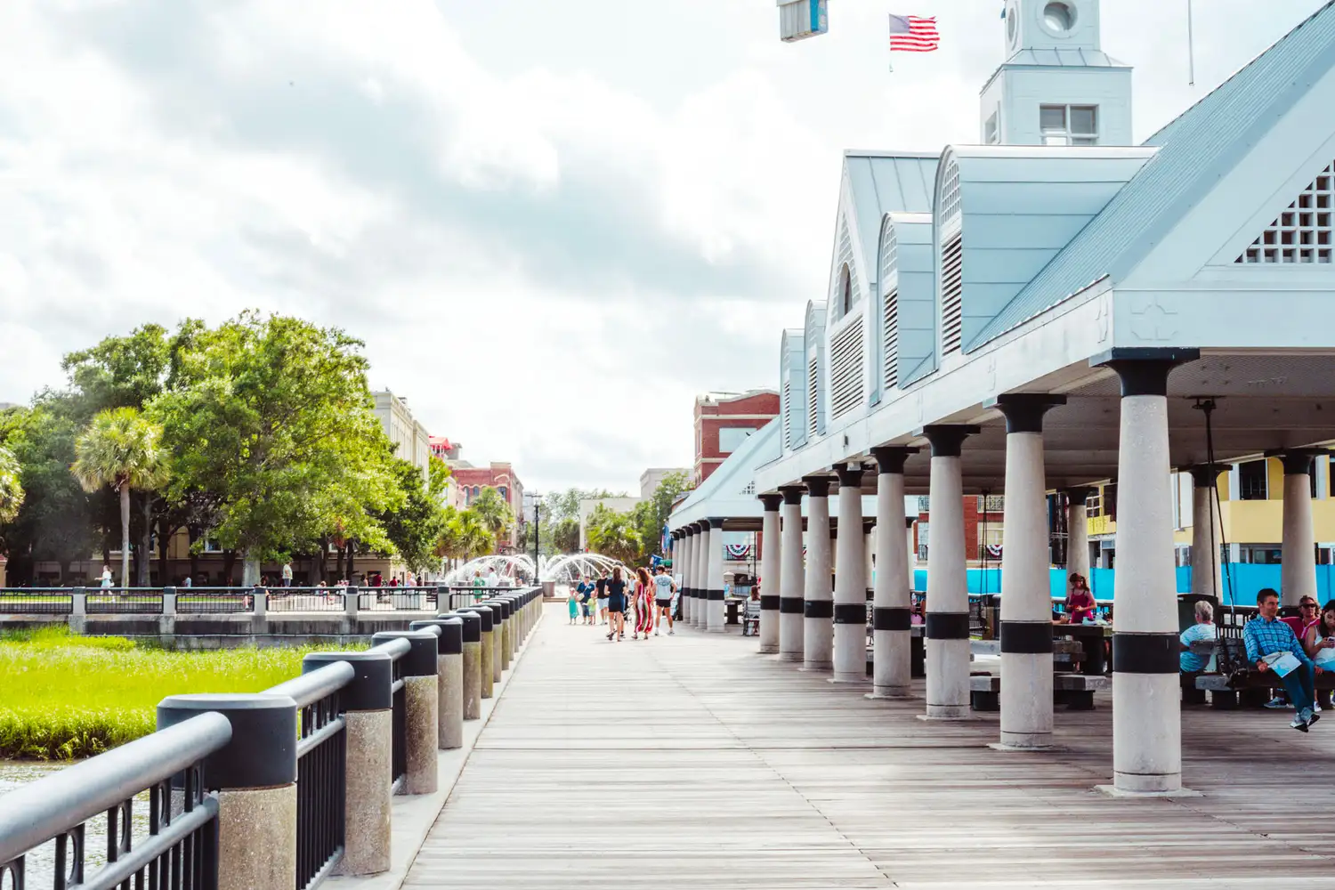 People walking along the waterfront boardwalk in Charleston, South Carolina, next to a white pavilion.