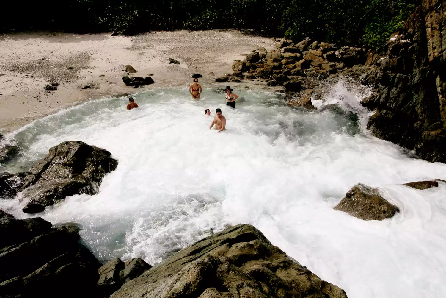 Travelers sitting in the foaming white water of a natural rock pool by the ocean.