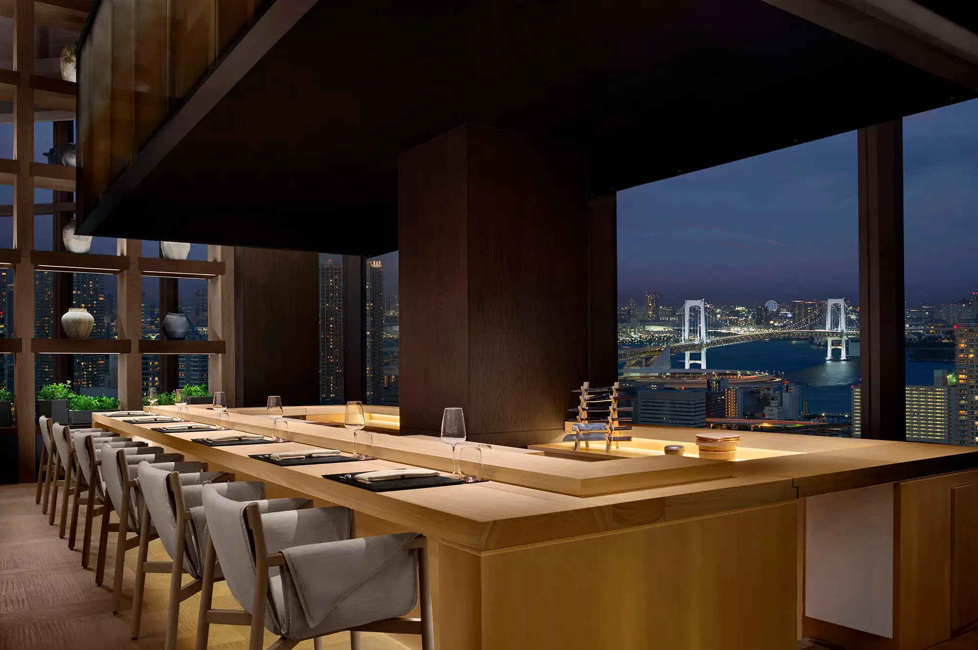 An upscale dining room at night with a view of a lit suspension bridge through the window.