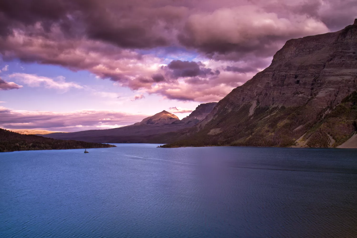 A vibrant sunset casting a golden glow over the mountains and reflective waters of St. Mary Lake.