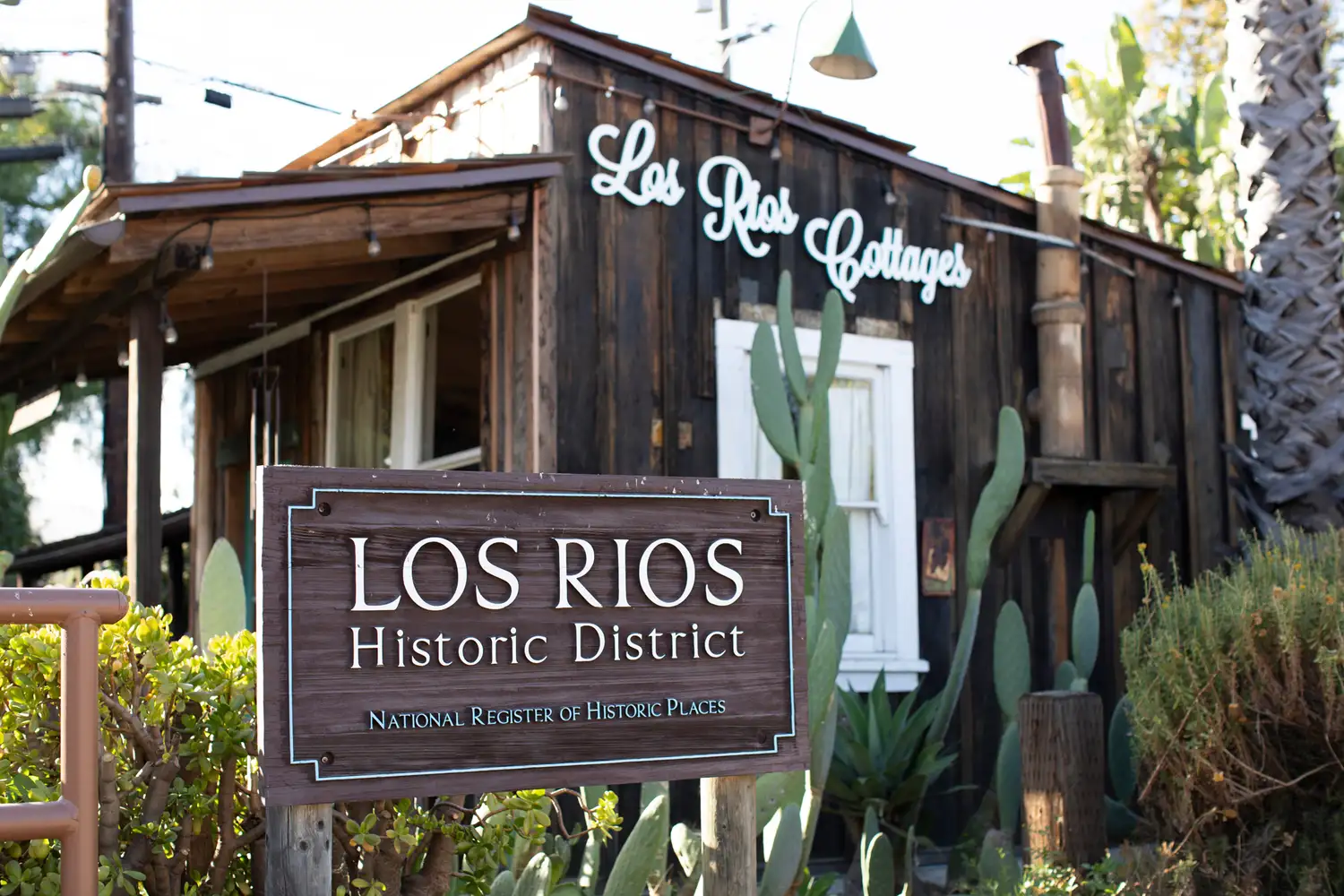 Entrance sign for the Los Rios Historic District with wooden cottages in the background.