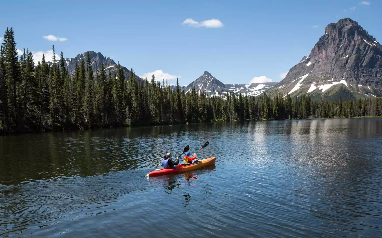 People paddling a canoe on the calm waters of Two Medicine Lake surrounded by mountains.