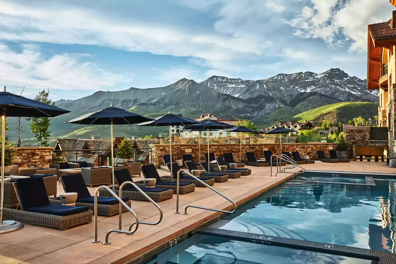 An outdoor swimming pool at Madeline Hotel overlooking lush green mountains during summer.