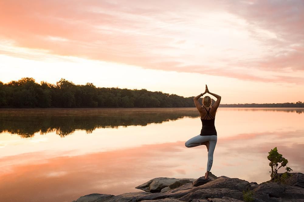A person practicing a yoga pose outdoors on the resort's green grounds under a large tree.